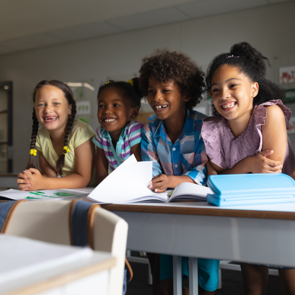 Happy multiracial elementary school students sitting at desk in